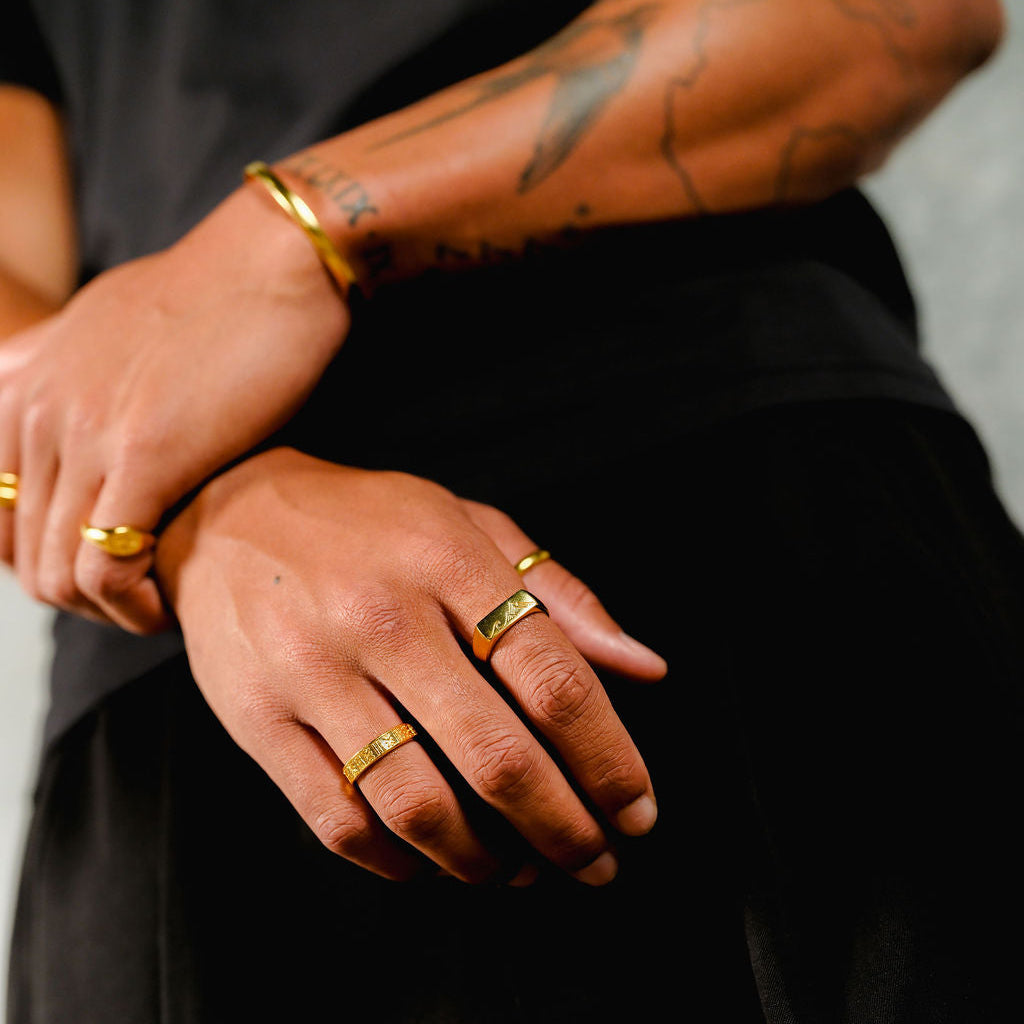 A close-up of a man's hands, styled with the Billie Jo Drifter and Union gold set. The 18k gold vermeil cuff and rings create a stacked, contemporary men's jewellery look.