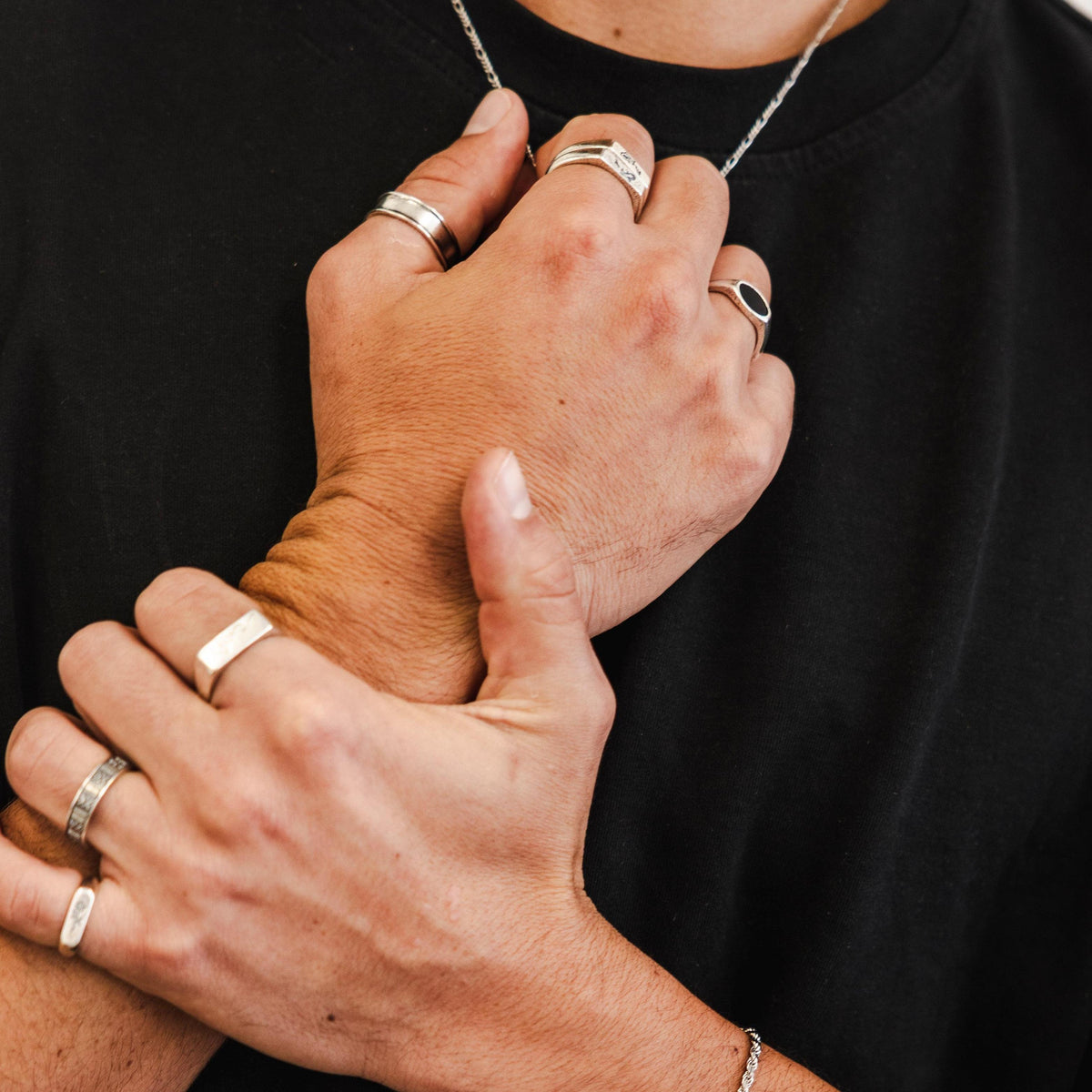 A man wearing the sterling silver Slim Figaro Necklace by Billie Jo, layered with multiple silver rings for a modern, masculine look. An example of how to style this classic piece.