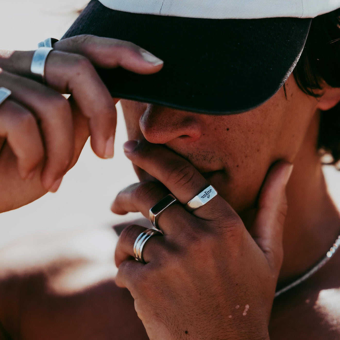 A close-up editorial shot of a man in a cap, his hands adorned with a variety of sterling silver Billie Jo Stacker Rings, capturing a modern and edgy style.