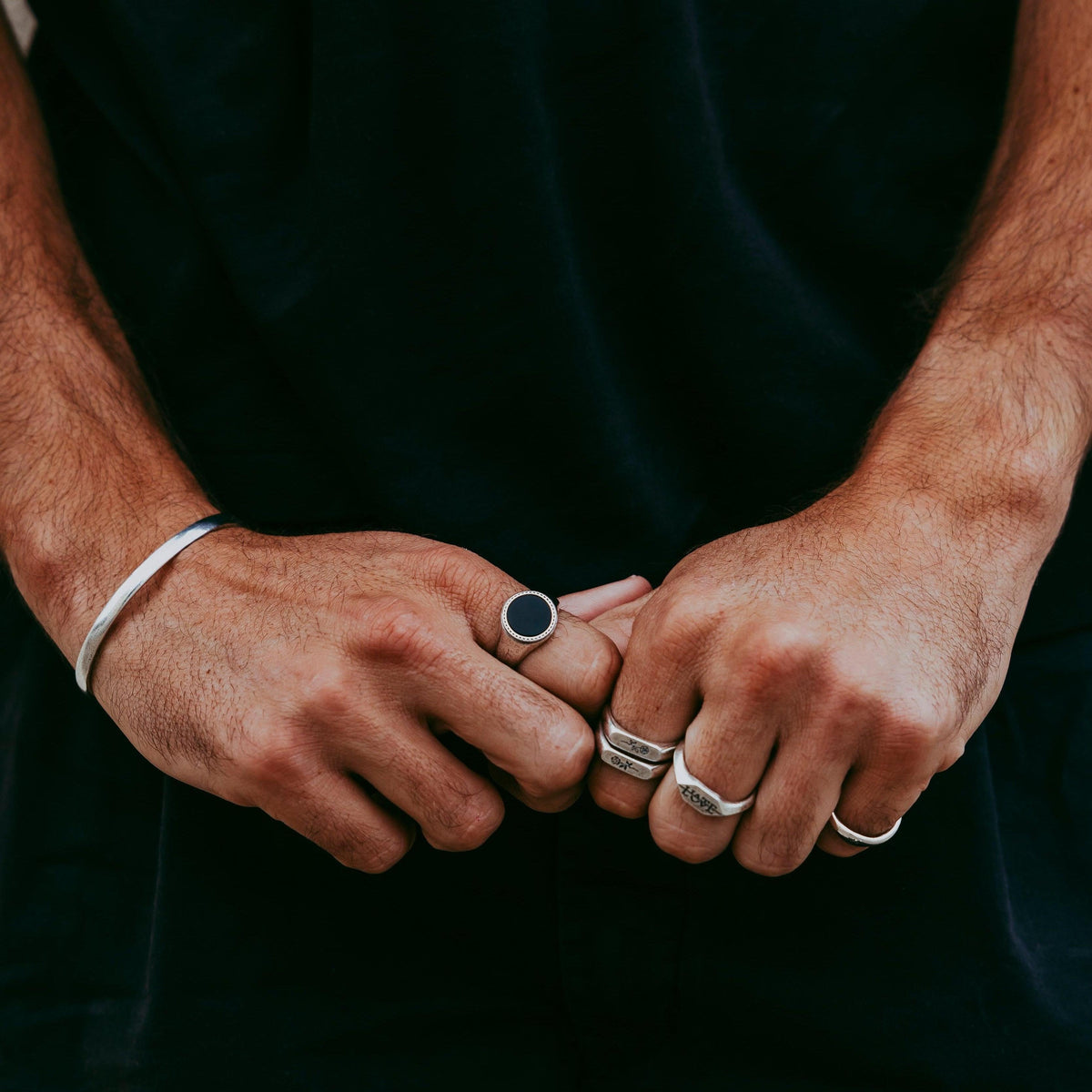 A man wearing a collection of sterling silver Billie Jo jewellery, including the Rosa Stacker rings, a cuff, and other signet rings for a modern look.
