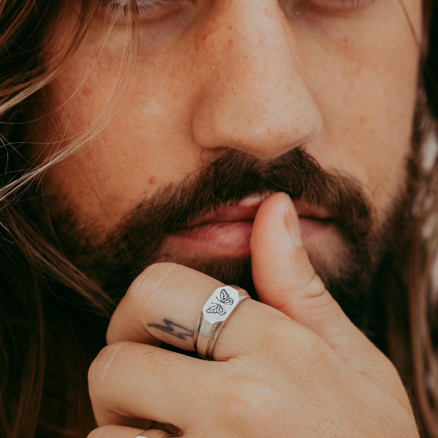 A close-up editorial shot of a model's face, with his hand and the Revival Ring partially covering his mouth, from Australian brand Billie Jo.