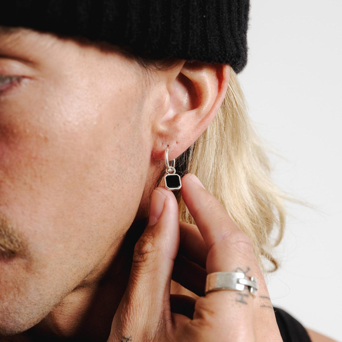 Male model touching the black stone of his Billie Jo Nox Earring in a close-up editorial portrait
