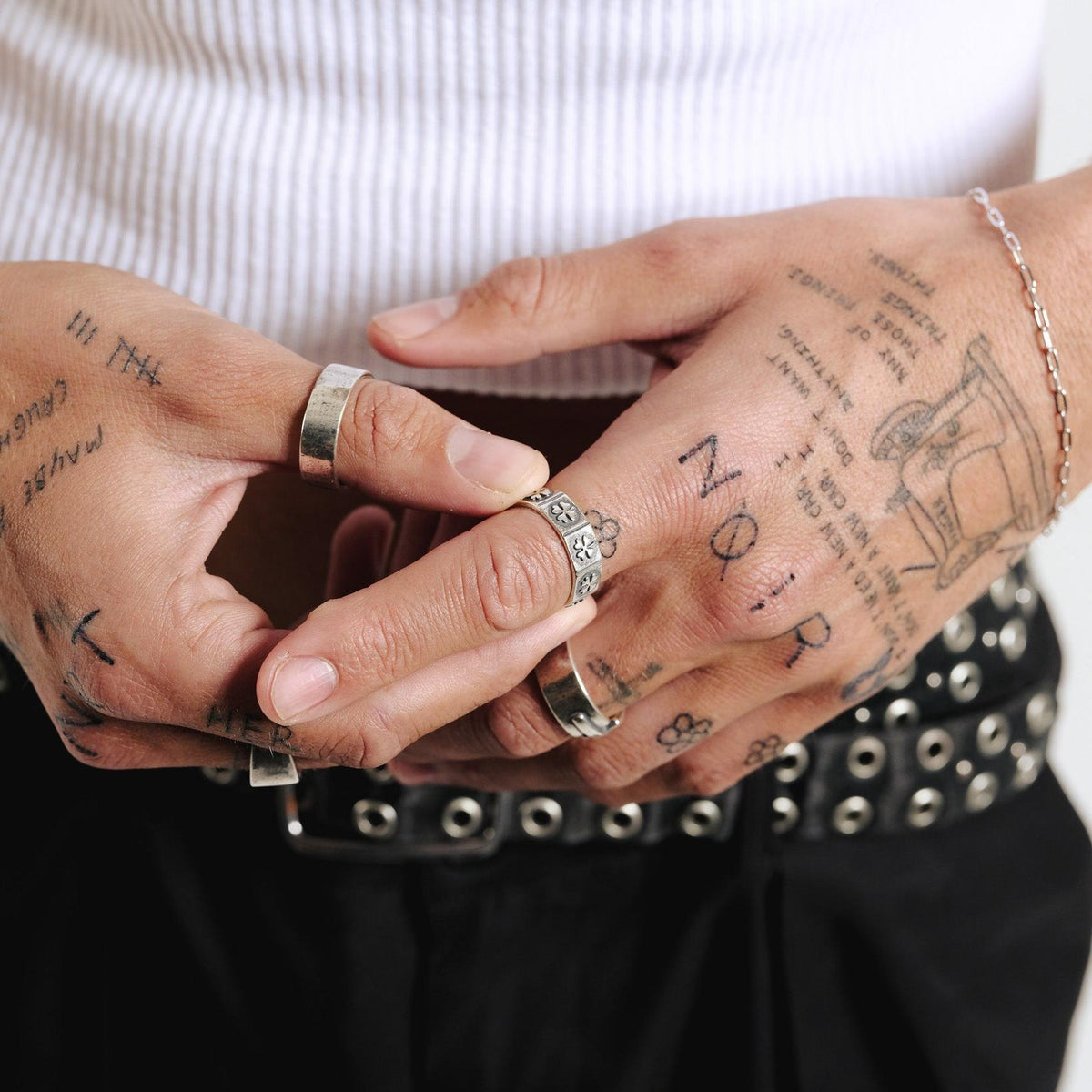 A man with tattooed hands wears the Billie Jo Slim Link Bracelet, paired with several silver rings, a white tank top, and a black leather belt.