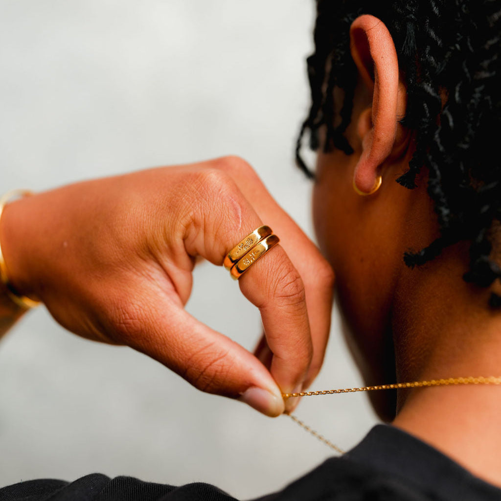 A close-up of a man wearing the Billie Jo Rosa Stacker rings in gold while adjusting a delicate gold chain necklace, showcasing the jewellery's versatility.
