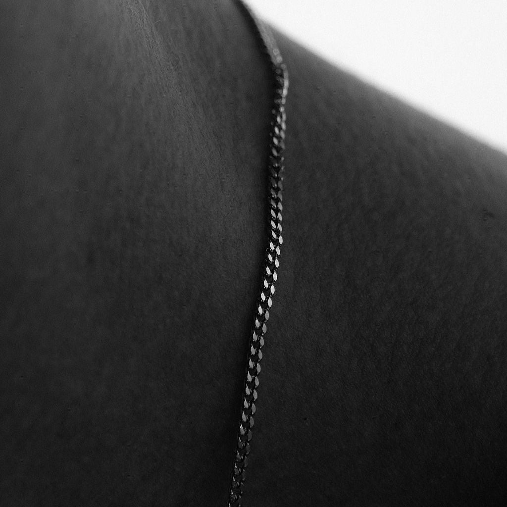 A detailed black and white shot of the Curb Necklace, highlighting the texture and form of the sterling silver chain against the skin.