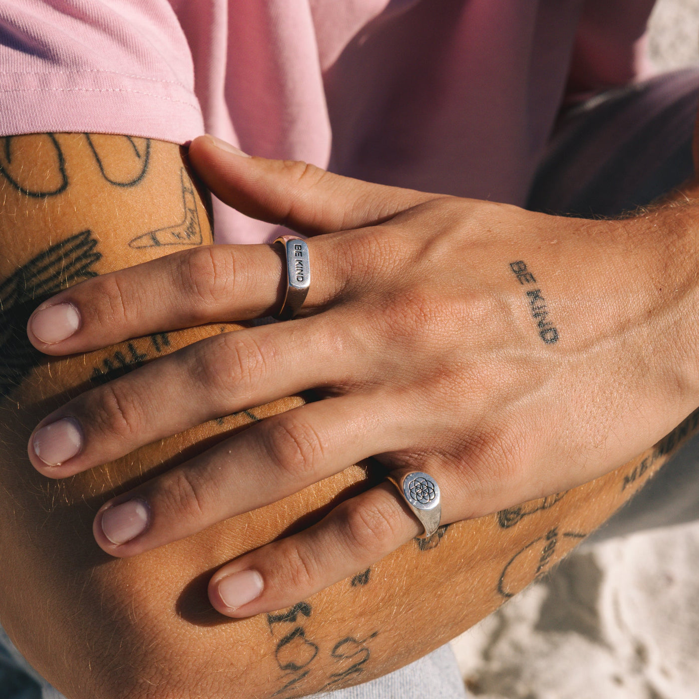 On-hand shot of the BE KIND ring from Billie Jo, worn by a man with tattoos on a sunny day, showcasing its casual and stylish vibe.