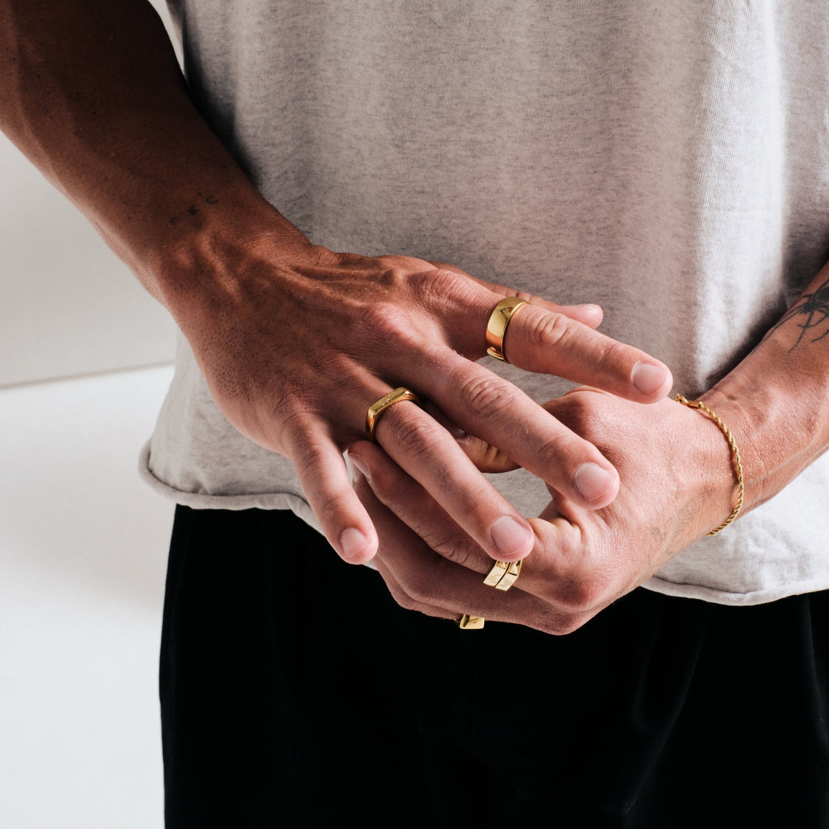 Men's Gold Canvas Ring in 18k gold infused stainless steel, worn on the index finger, hands clasped at his waist