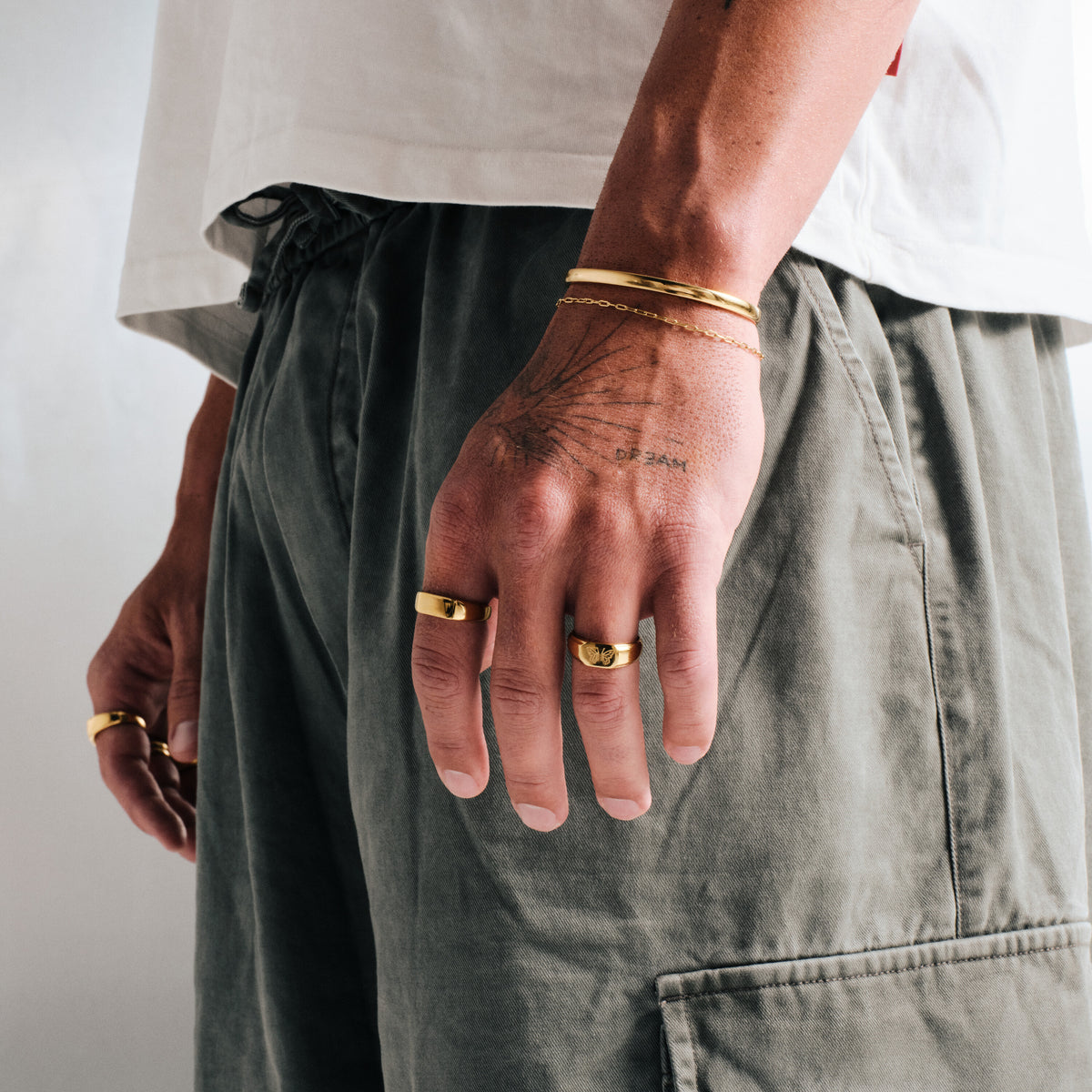 Men's Gold Drifter Cuff in 18k gold infused stainless steel, worn on his left wrist, hand by his side, white tee, olive pants