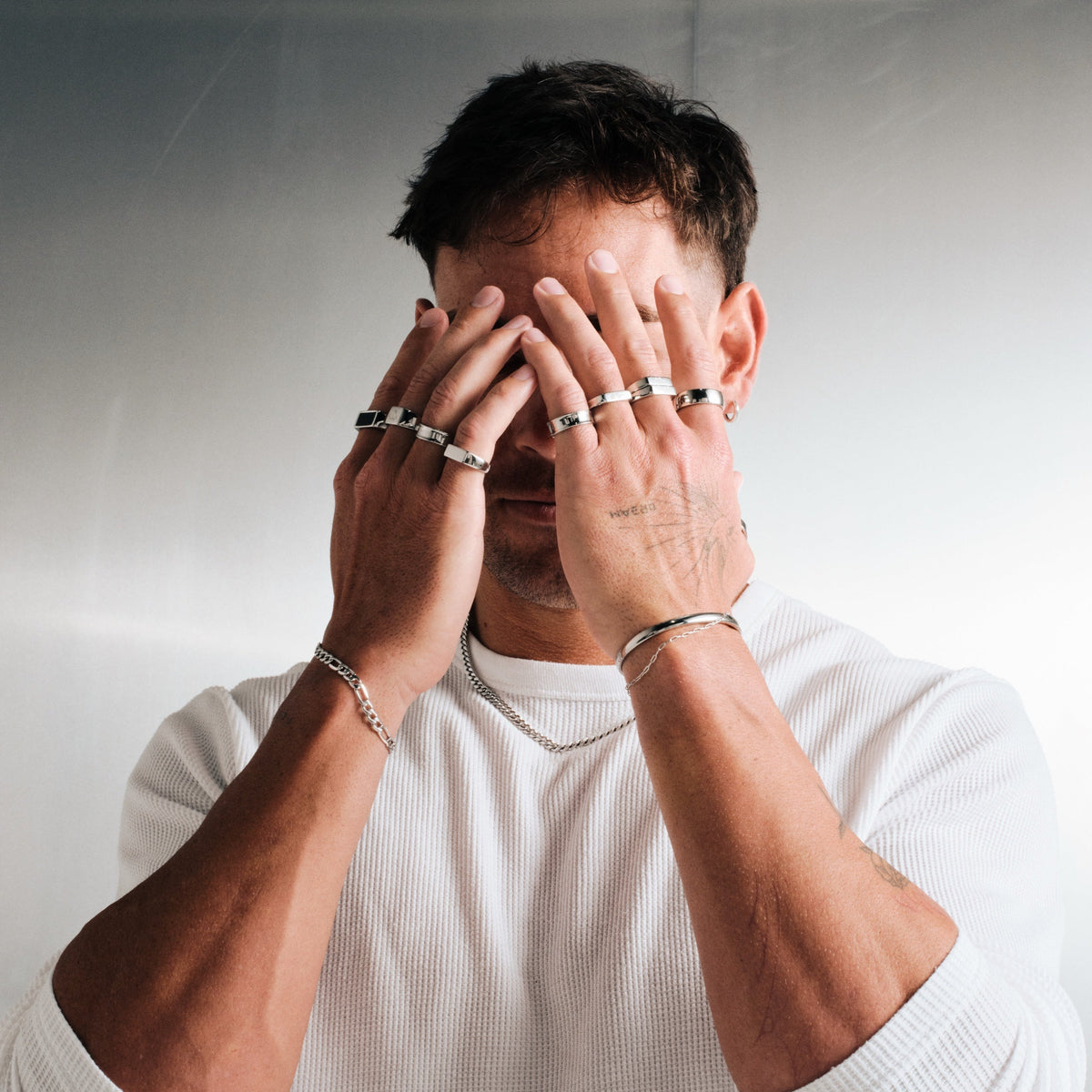 Men's Genesis Ring in 316L stainless steel, silver finish, in a stack, hands covering his face, white waffle tee