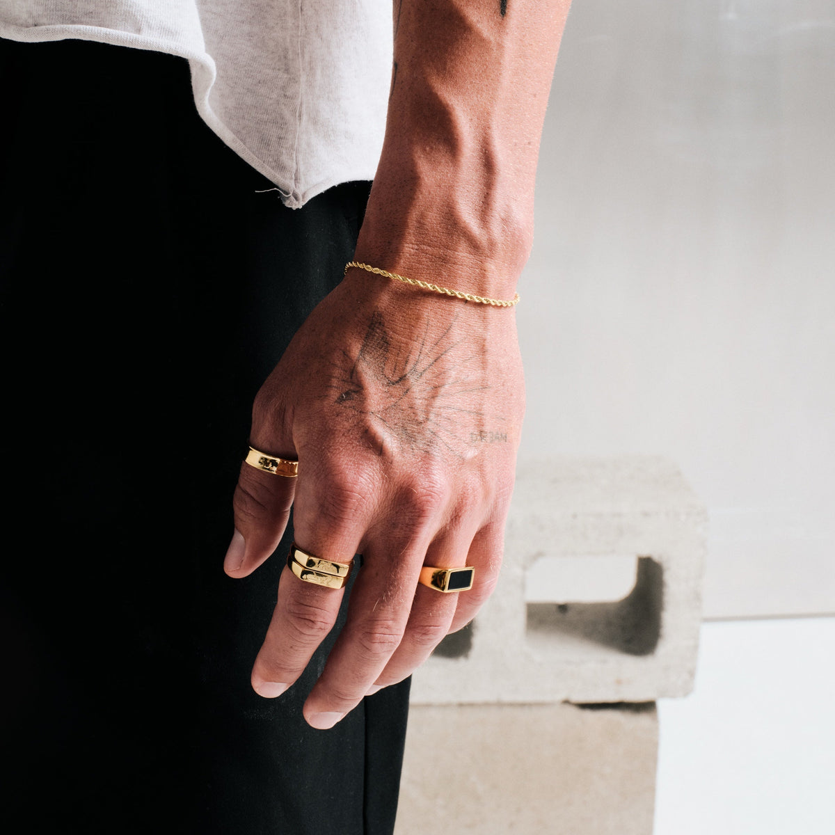 Men's Gold Onyx Ring in 18k gold infused stainless steel, in a stack, hand by his side, concrete block behind