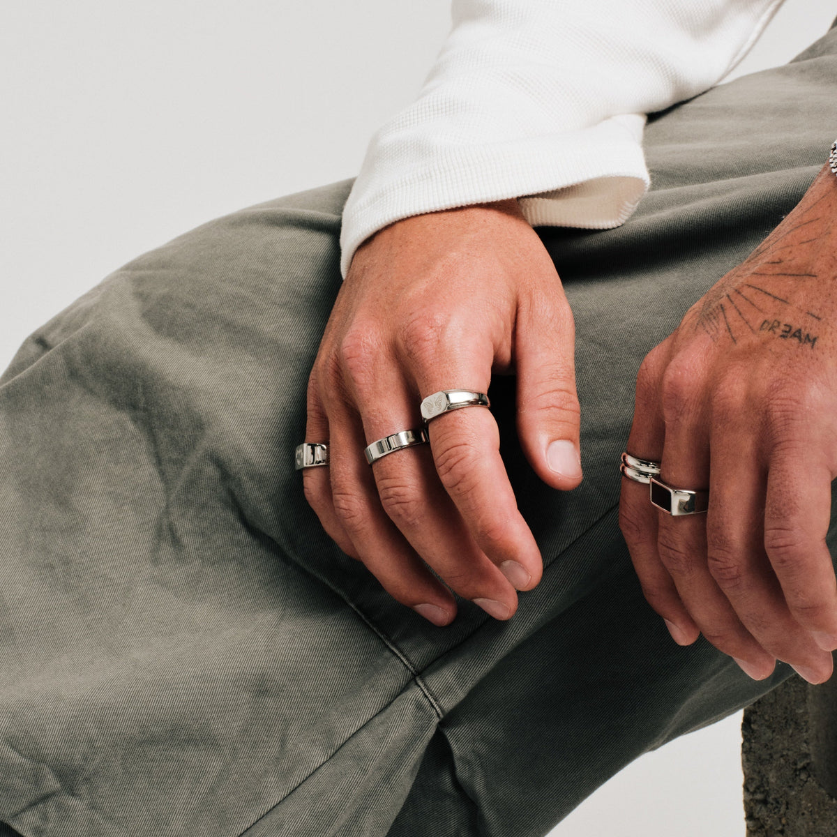 Men's Revival Ring in 316L stainless steel, silver finish, worn on his right index finger, seated, hands resting on knees