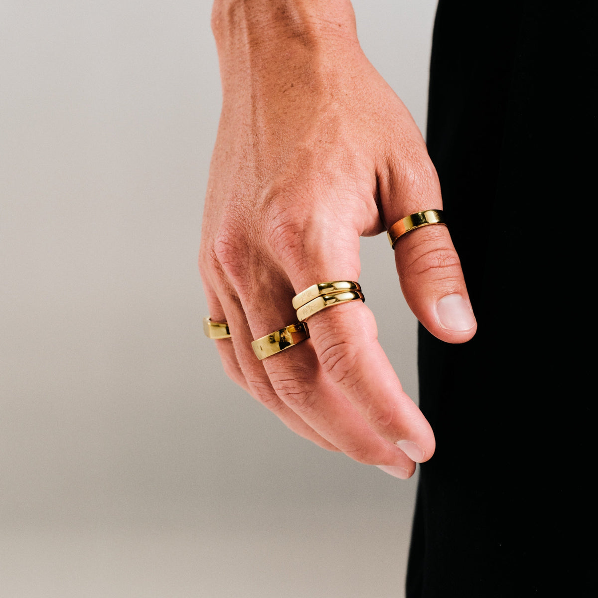 Men's Gold Rosa Stackers in 18k gold infused stainless steel, worn on his right index finger, hand hanging by his side