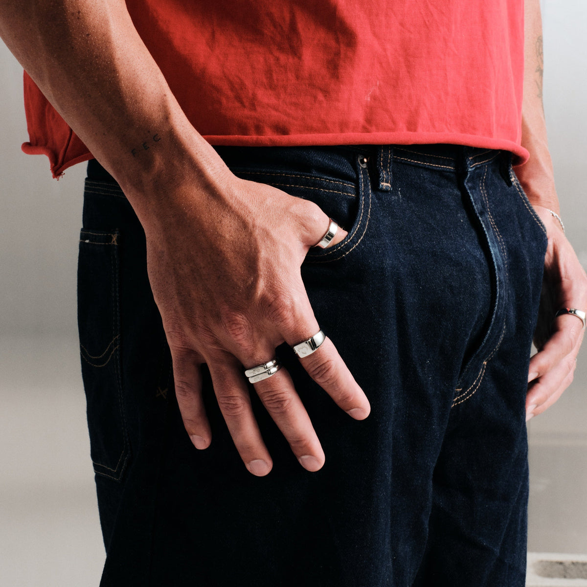 Men's Rosa Stackers in 316L stainless steel, silver finish, worn on his right middle finger, thumb hooked in jeans pocket
