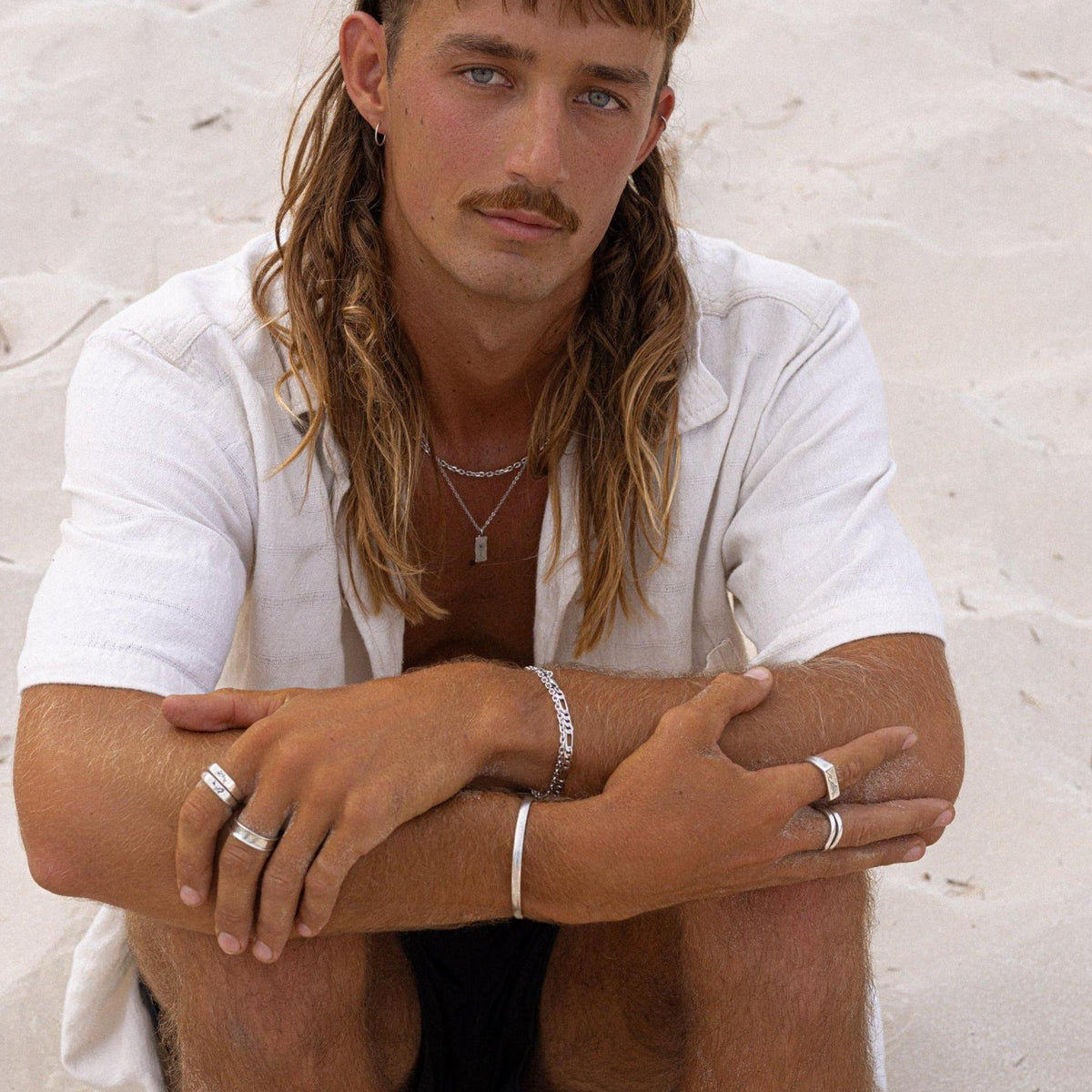 A male model with a mullet and moustache wears a white shirt and a selection of Billie Jo men’s jewellery, including the Union Ring. Editorial campaign shot.