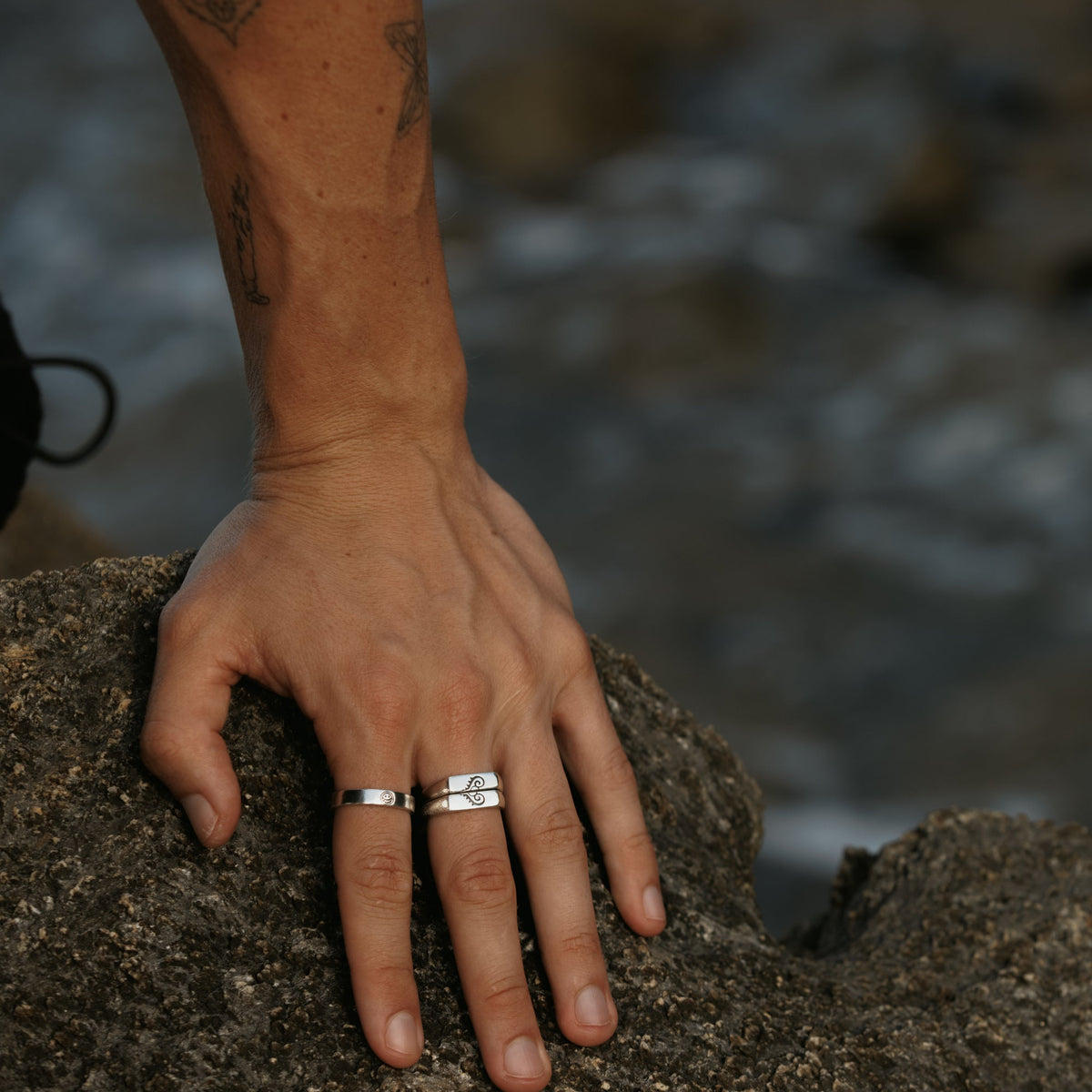 A man's hand resting on a rock, wearing the sterling silver Reflection Ring and a stacked ring from Australian jewellery brand Billie Jo. A modern, masculine look.