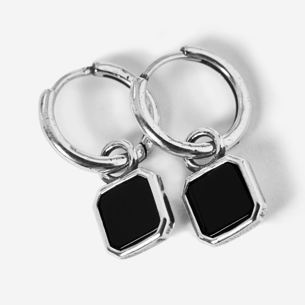 A pair of sterling silver Nox Earrings by Billie Jo, featuring a small huggie hoop with a dangling geometric black stone pendant on a clean white background.