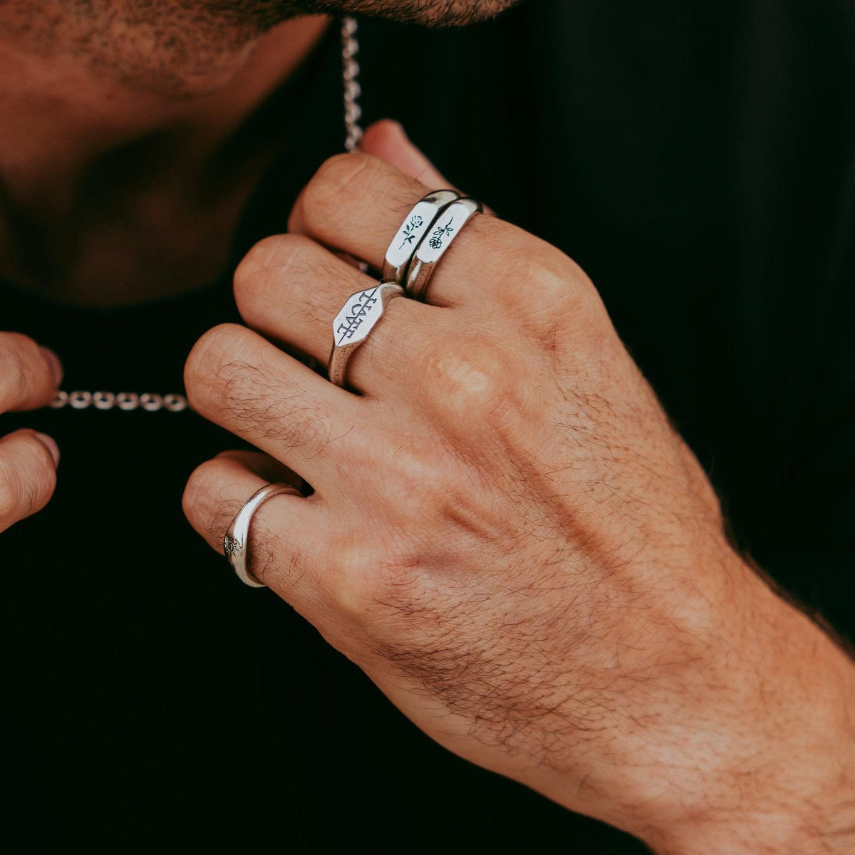 A man's hand wearing the sterling silver Rosa Stacker rings from Billie Jo, layered with other rings for a bold, masculine style.