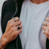 Man wearing the Abyss Ring with black onyx stone along with other silver rings and a necklace, styled with a casual outfit