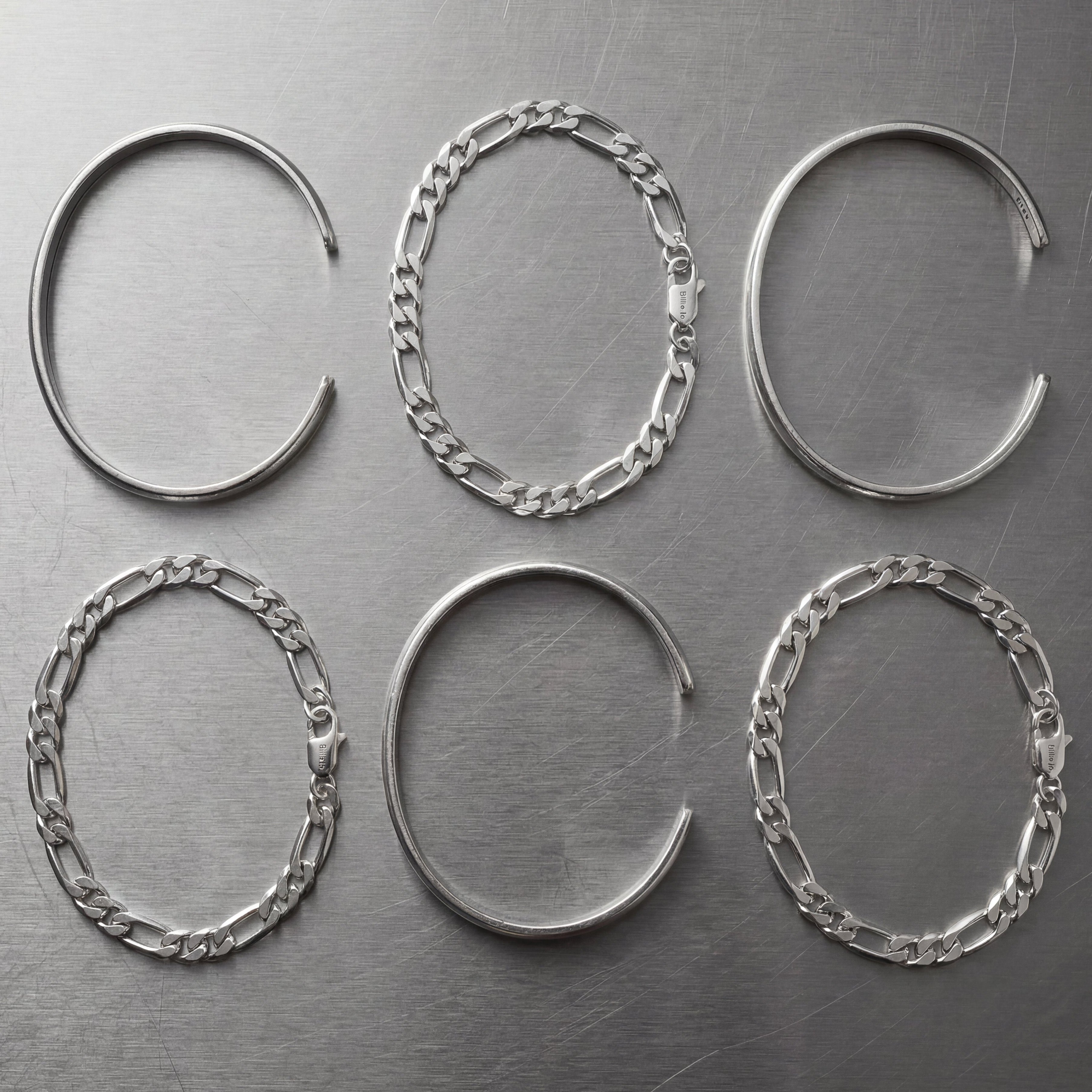 Set of six silver cuffs and figaro bracelets on a stainless steel bench top