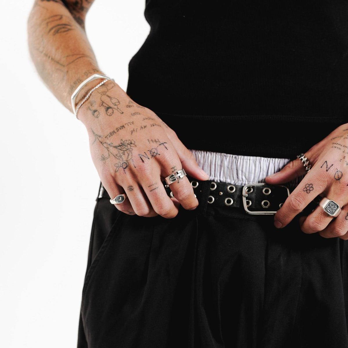 A close-up lifestyle shot of a man wearing the Billie Jo Bind Ring. The sterling silver ring is styled with other silver rings, a black tank top, and black trousers, creating a masculine, editorial look.