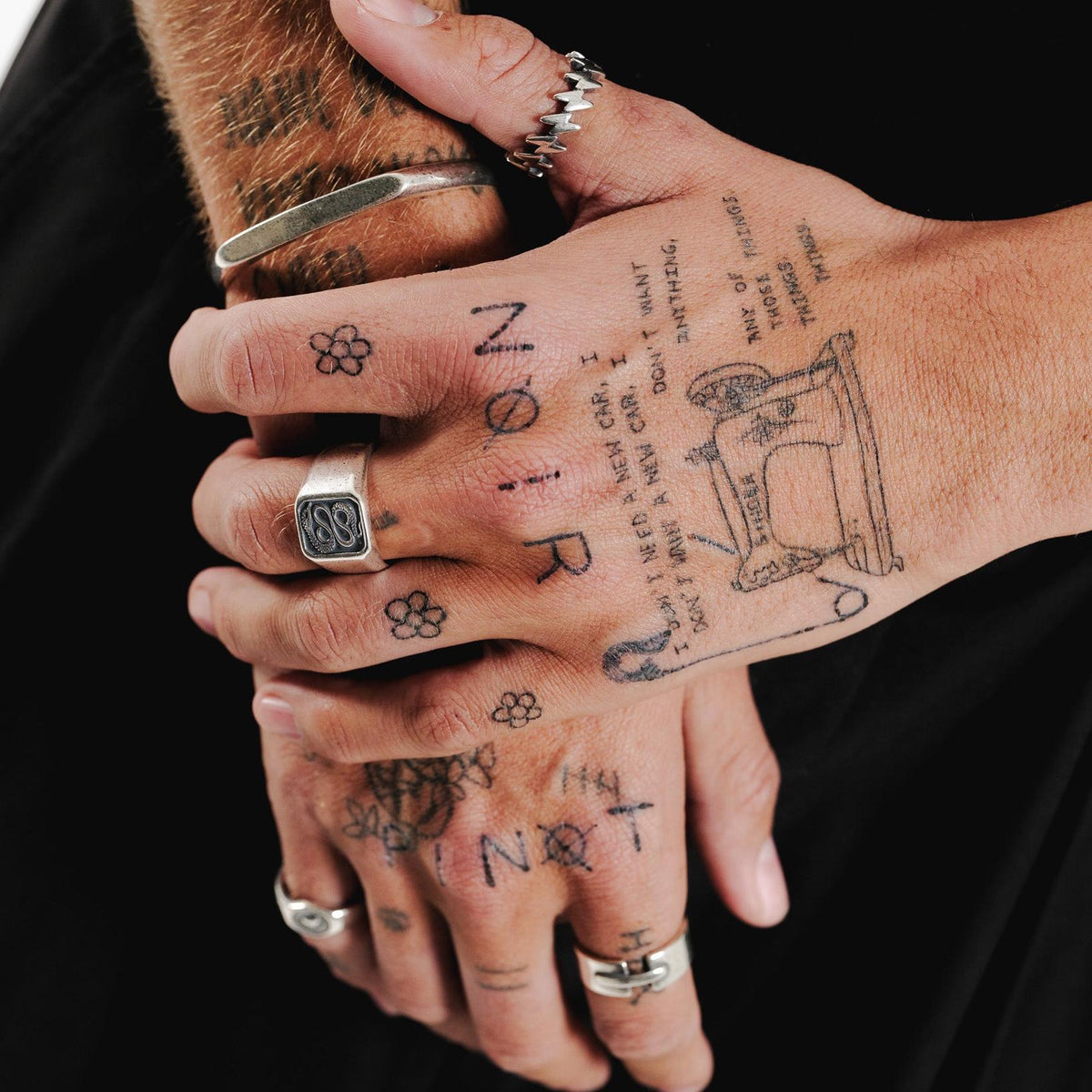 A close-up lifestyle shot of the Billie Jo Serpent Ring on a tattooed hand, paired with a silver cuff and other rings for a complete look.