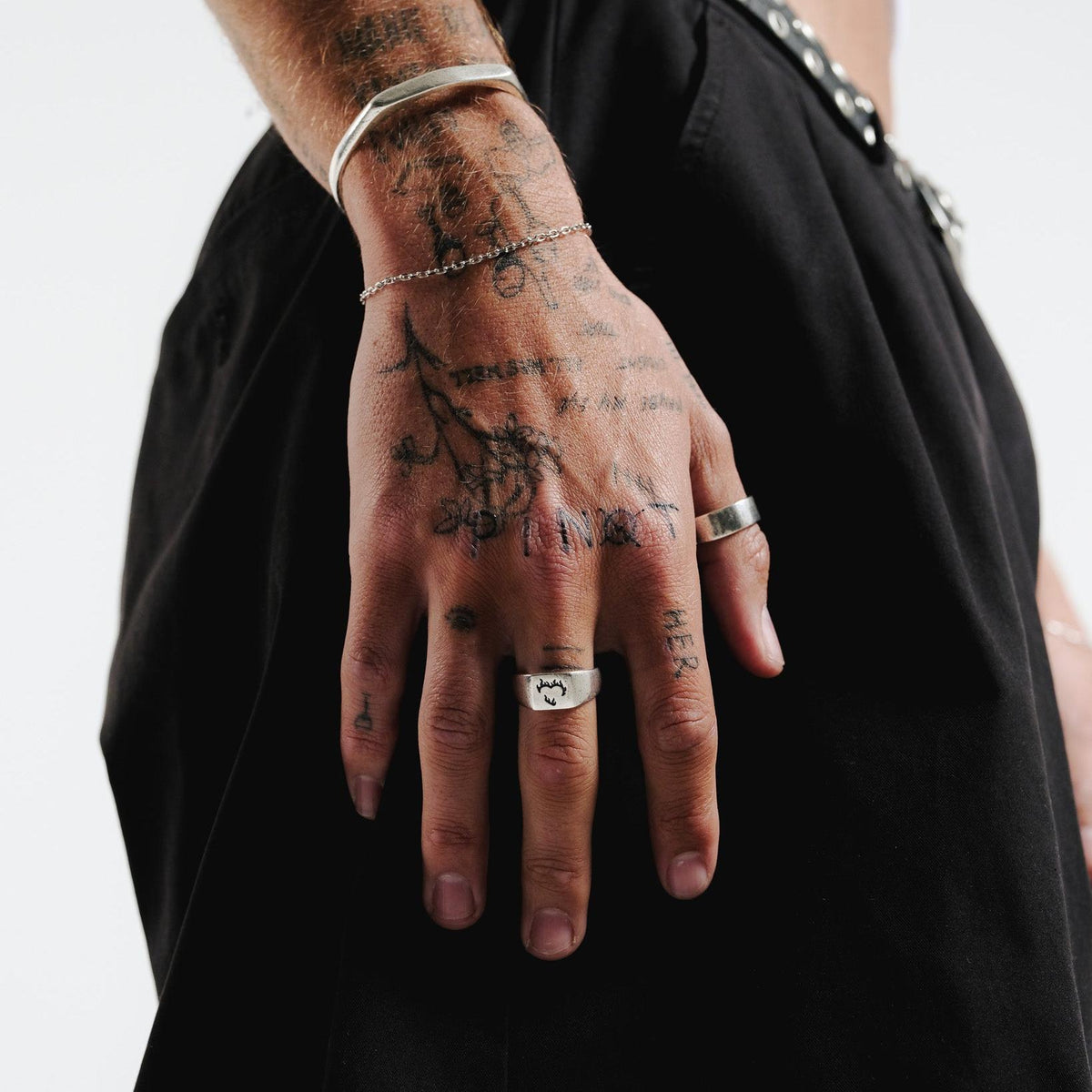 A close-up of a man's tattooed hand wearing the Billie Jo Echo Cuff in sterling silver, paired with a delicate chain and two minimalist silver rings. This image highlights the cuff's versatility and modern style.