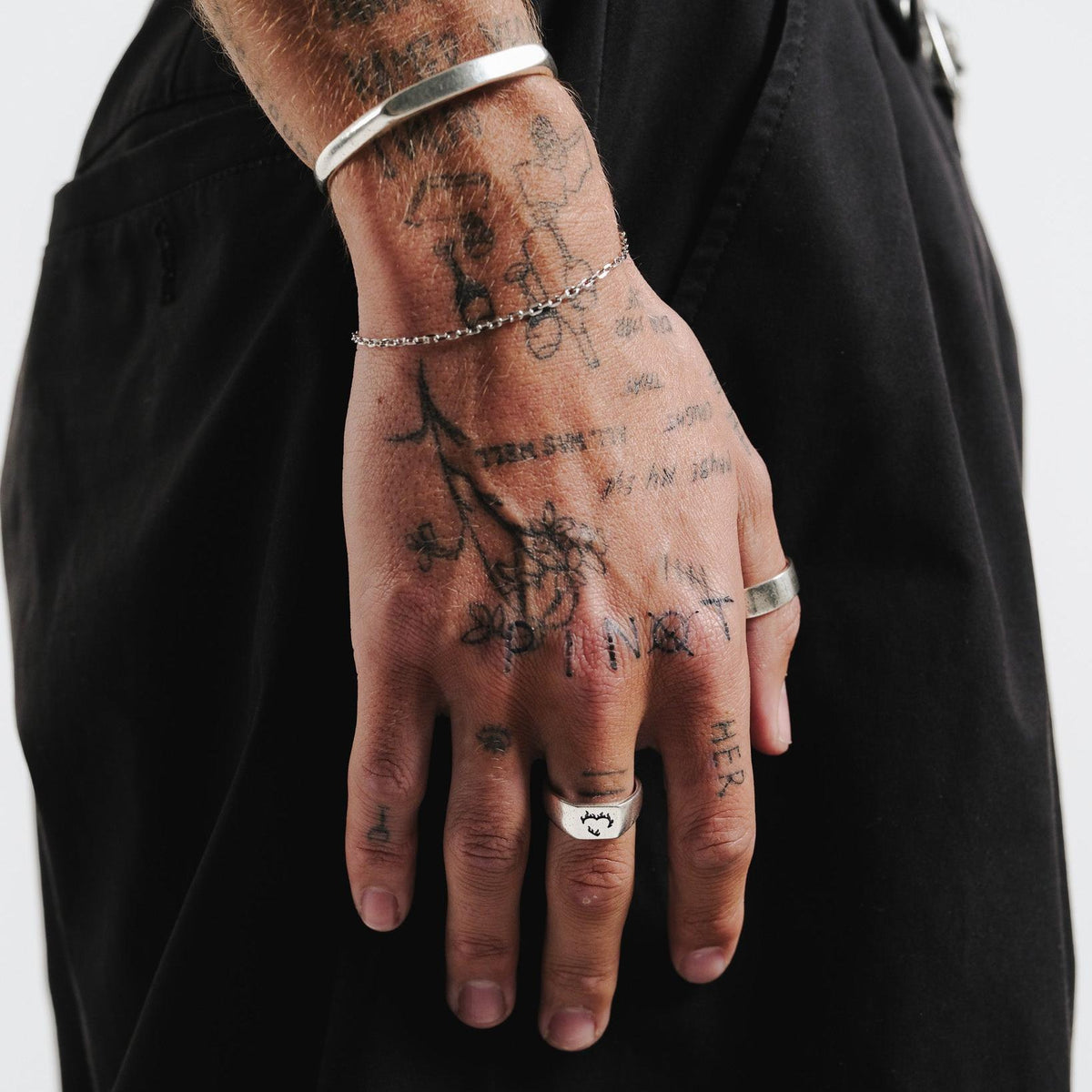 A tattooed man's hand wearing the sterling silver Slim Batch Bracelet from Billie Jo, styled with a silver cuff and rings for a modern, layered look.