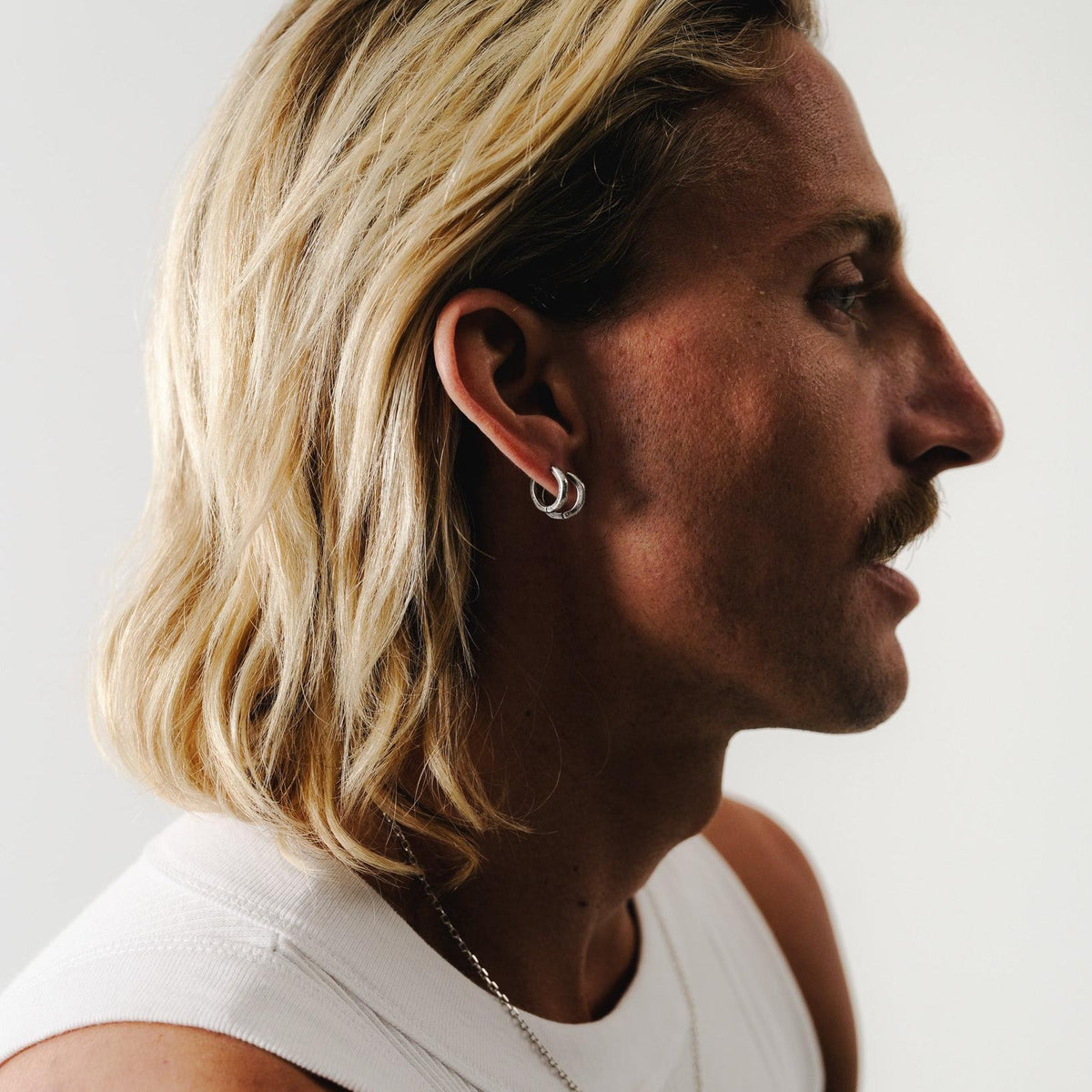 A stylish profile shot of a man with blonde hair and a moustache, wearing a stack of two sterling silver Billie Jo Lumina hoop earrings.