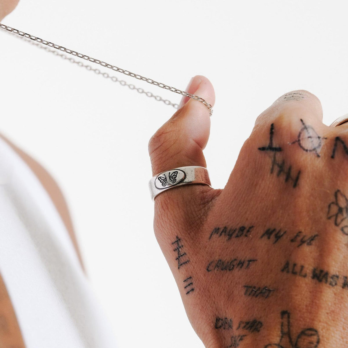 Close-up of the Slim Batch Necklace chain by Billie Jo, held by a man with hand tattoos, showcasing the fine craftsmanship of the silver links.