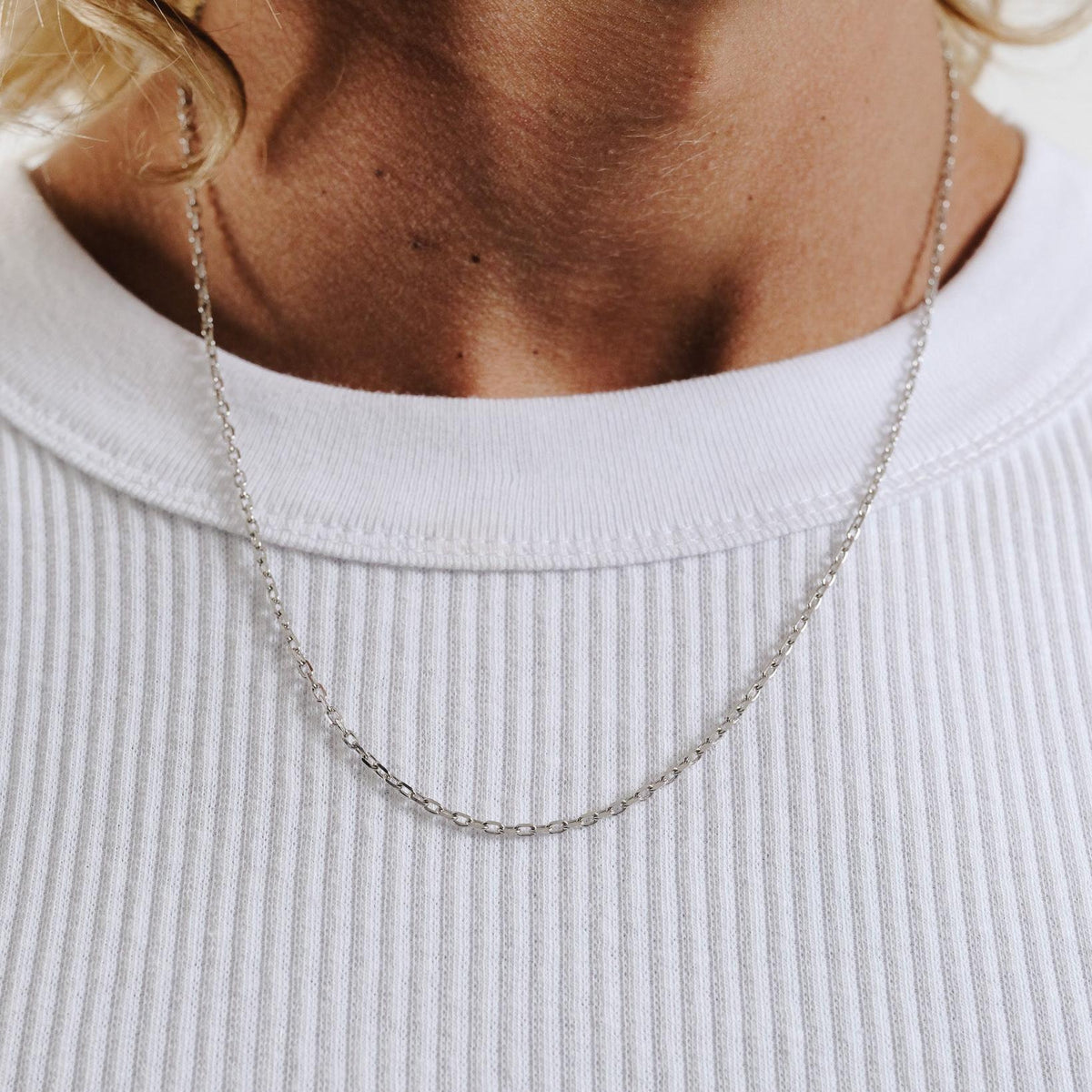 A man wearing the sterling silver Slim Batch Necklace from Billie Jo, styled with a simple white ribbed tank top for a modern, everyday look.