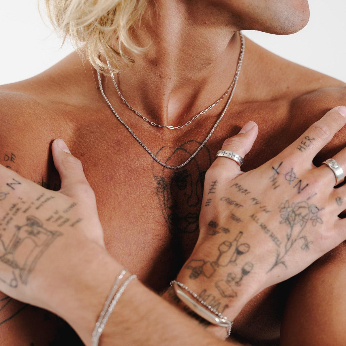 A man with tattooed hands and arms showcases the layered look of the sterling silver Slim Link Necklace from Australian jewellery brand Billie Jo.