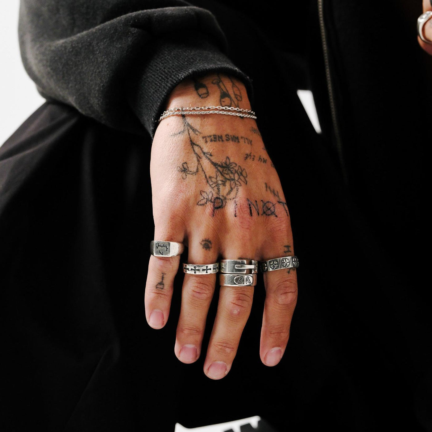 A close-up on a man's tattooed hand, showcasing a curated selection of sterling silver rings, including the distinctive Billie Jo LUCKY RING.