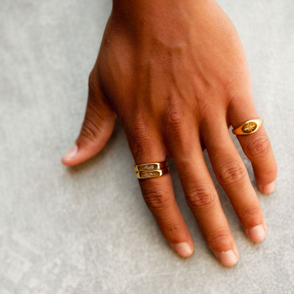 A man wears two gold Rosa Stacker rings from Billie Jo on his ring finger, styled with another gold signet ring on his index finger for a modern look.