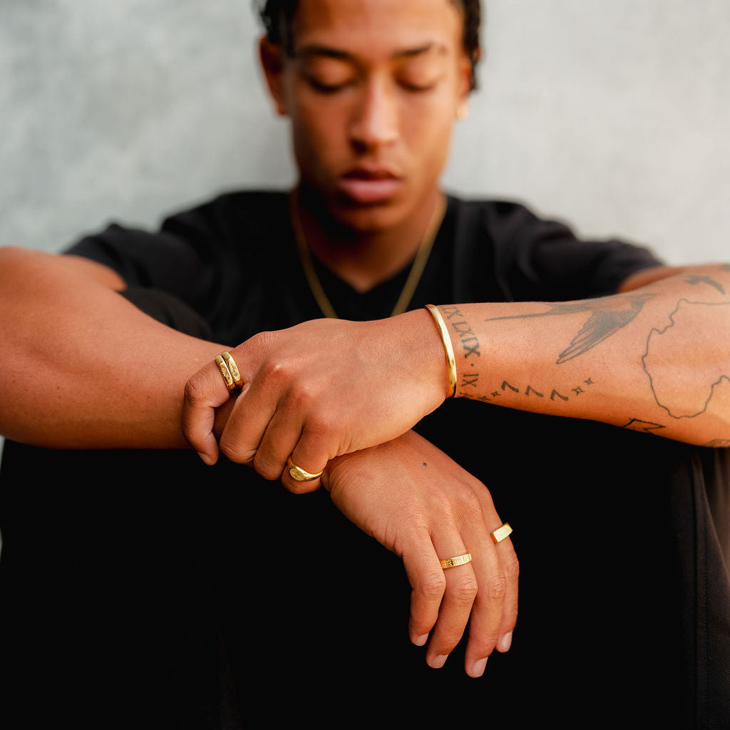 A man with his eyes closed, wearing the gold Rosa Stacker rings and other gold jewellery from Billie Jo, creating a relaxed and stylish look.