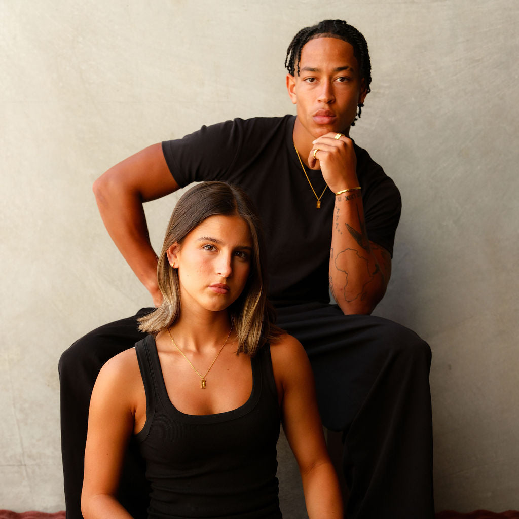 A male and female model both wear the gold Paradiso Pendant from Billie Jo, showcasing the versatile styling of this Australian-designed men's jewellery piece.