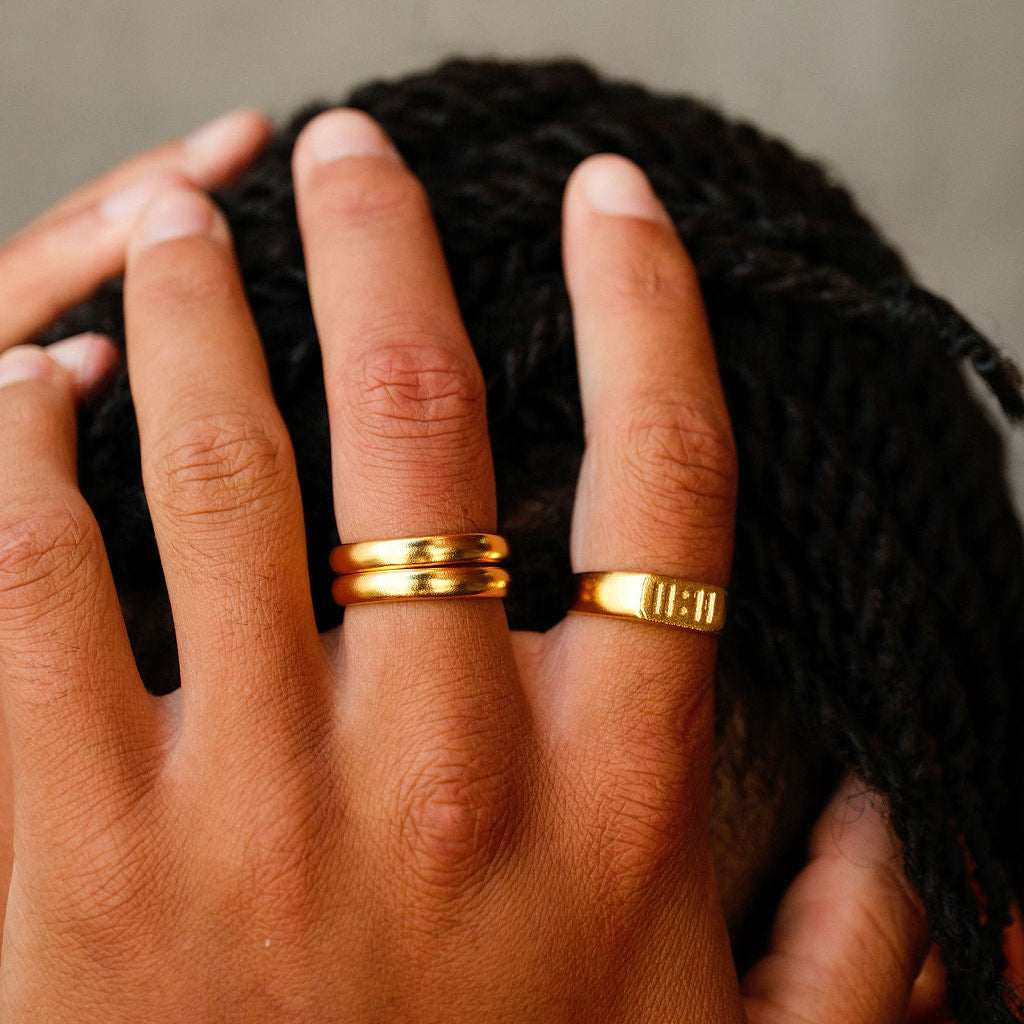 A close-up of a man's hand with two Billie Jo Stacker Rings in gold, running through his hair. The image showcases the stylish simplicity of the rings.