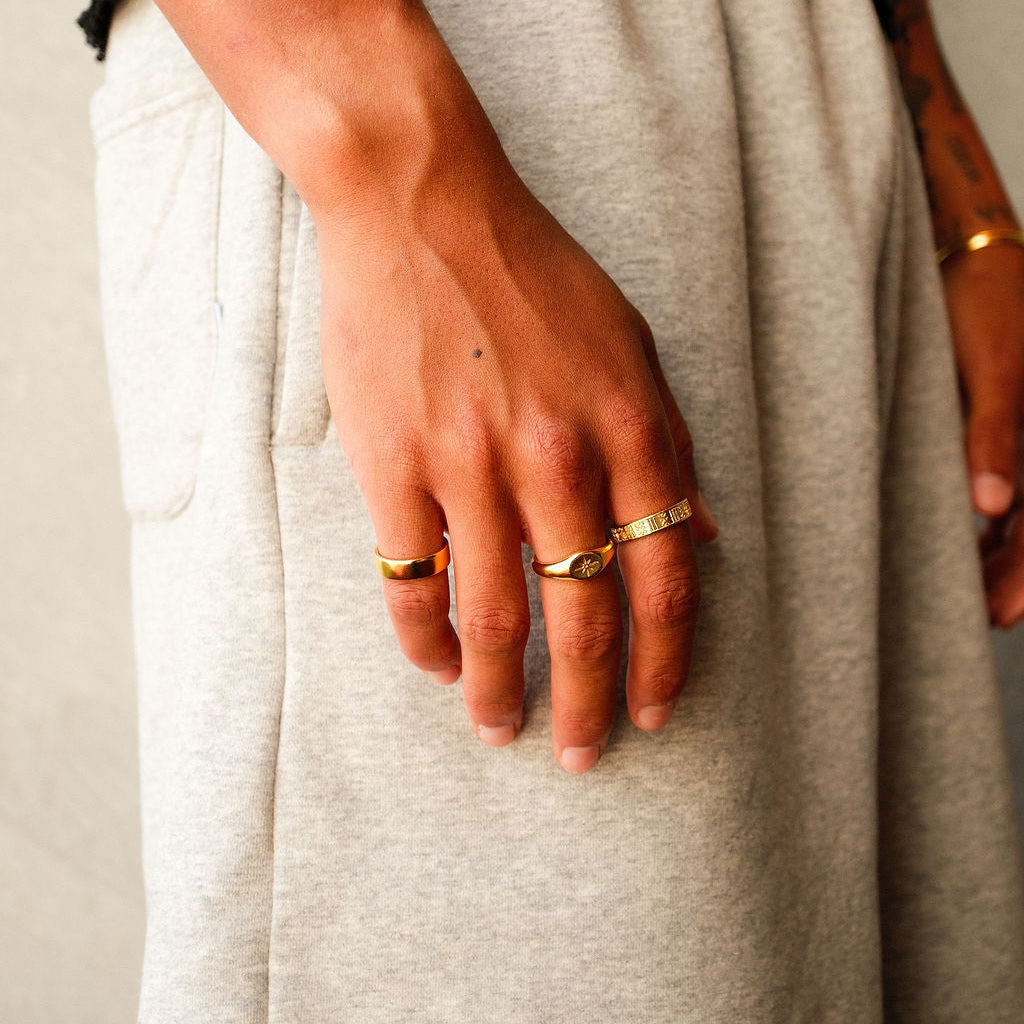 The Billie Jo Serenity Ring in gold worn on a man's hand against a casual grey fabric, highlighting the ring's versatile and modern design.