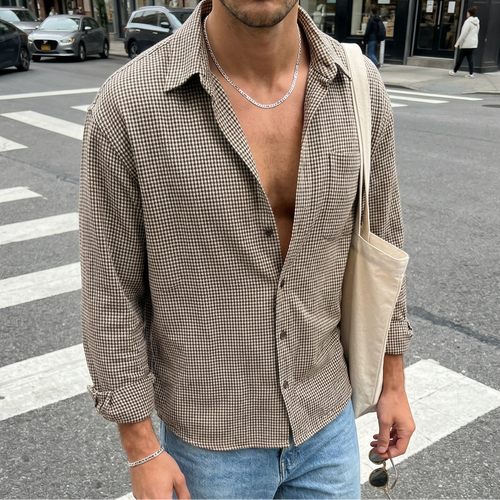 Man walking on a city street wearing an open shirt, jeans and figaro necklace