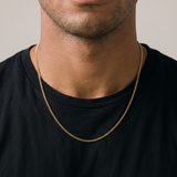 Man wearing a black t-shirt and gold chain, sitting against a beige background