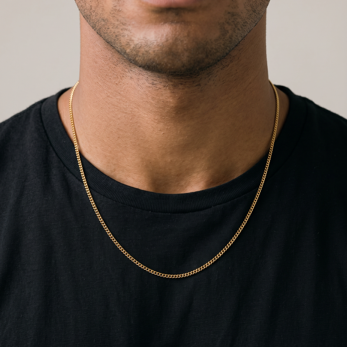 Man wearing a black t-shirt and gold chain, sitting against a beige background