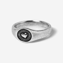 A 45-degree product shot of the sterling silver Vita Ring by Billie Jo. The signet-style ring features a central heart emblem with radiating sunbeam engravings, showcasing its textured, oxidised finish.