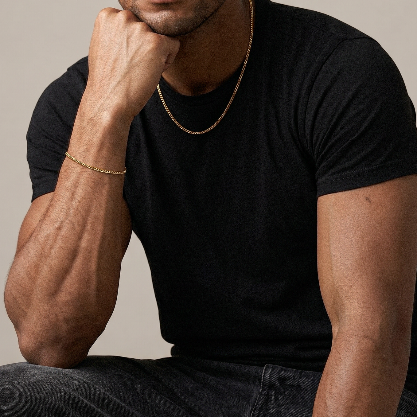 Man wearing a black t-shirt and gold chain, sitting against a beige background