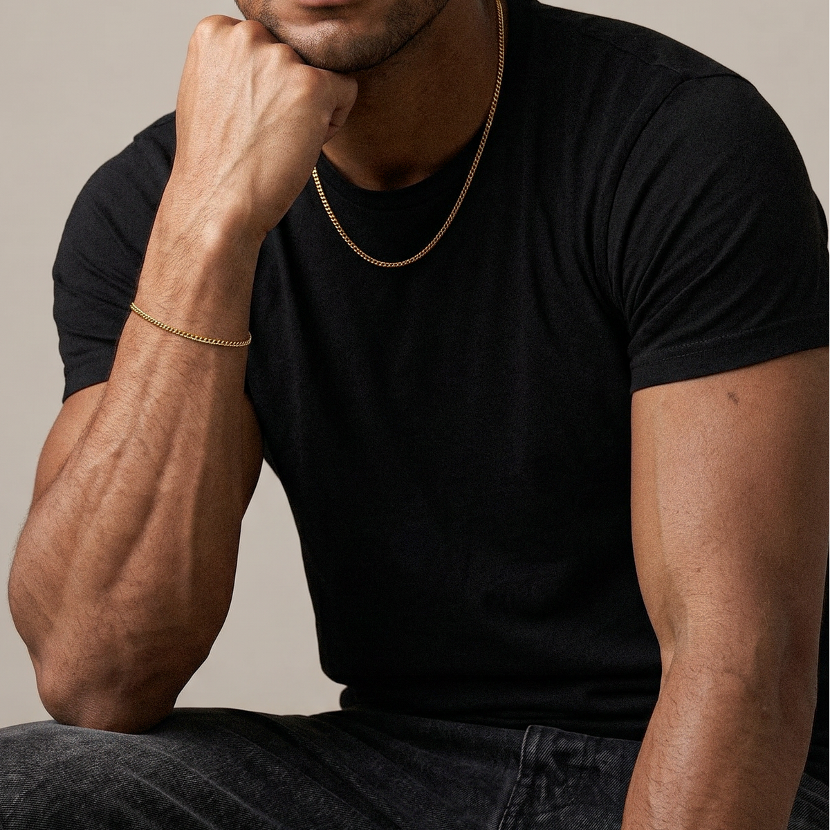 Man wearing a black t-shirt and gold chain, sitting against a beige background