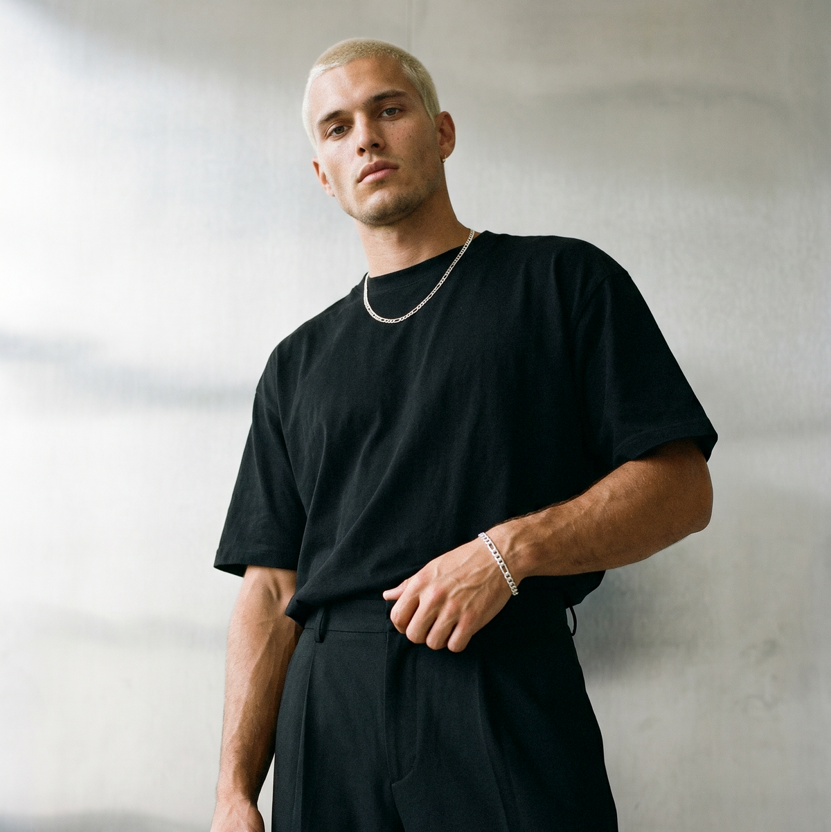 A male model wearing a polished silver tone stainless steel Figaro chain bracelet from Australian jewellery brand Billie Jo, photographed against a sleek silver chrome backdrop for everyday wear
