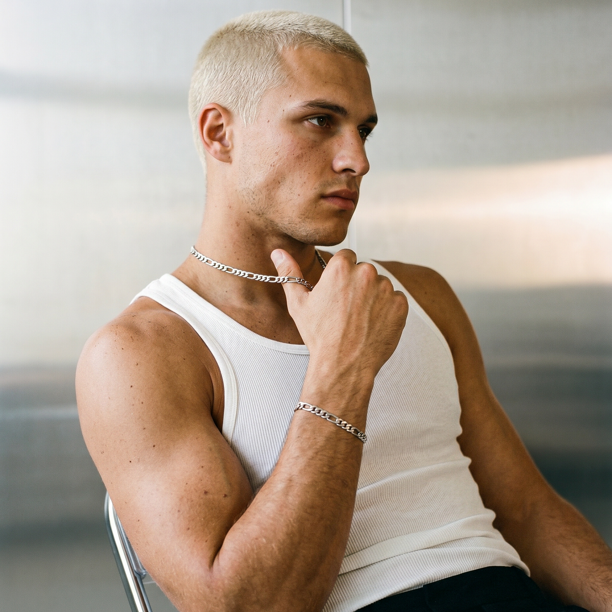 A man wearing a stainless steel men's Figaro chain bracelet from Australian jewellery brand Billie Jo, shot against a silver chrome background highlighting the thick bold alternating link design