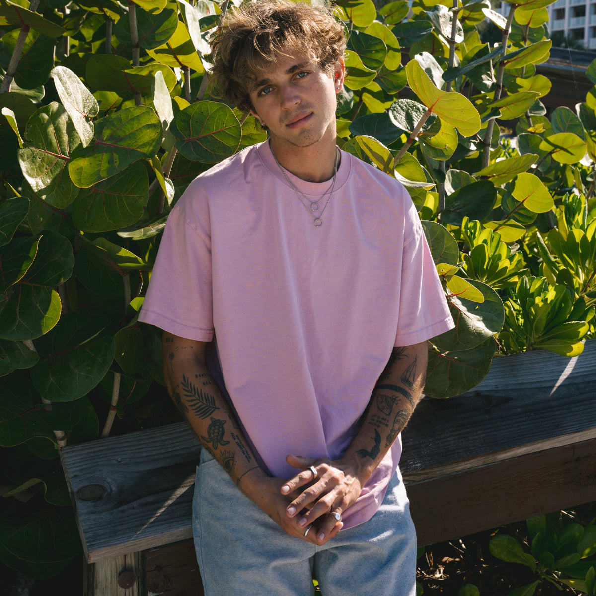 Campaign image for Billie Jo showing a model in a pink tee and the Ouroboros Pendant, standing against lush green foliage on the Gold Coast, Australia.