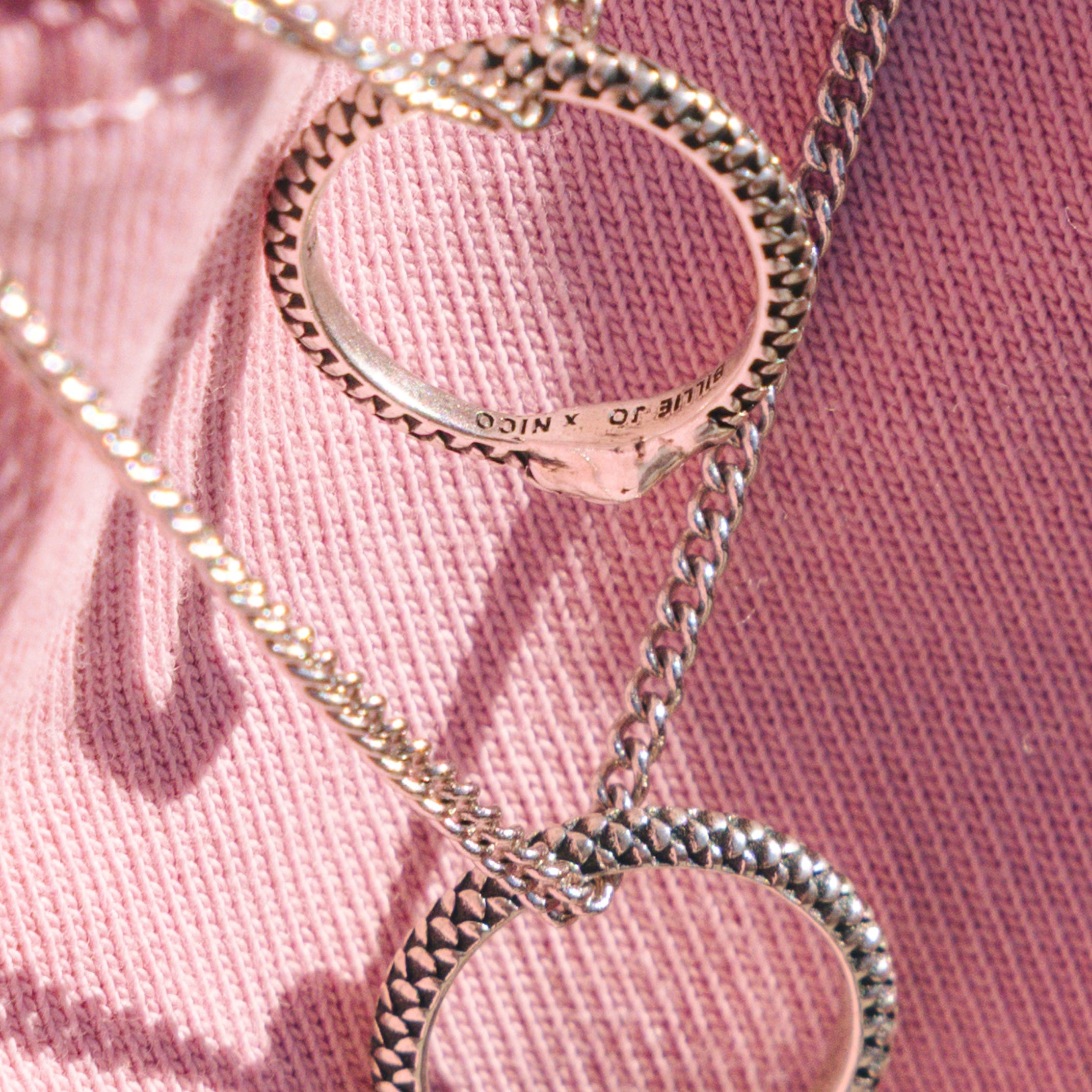 Silver necklaces with snake-shaped pendants on a pink fabric background