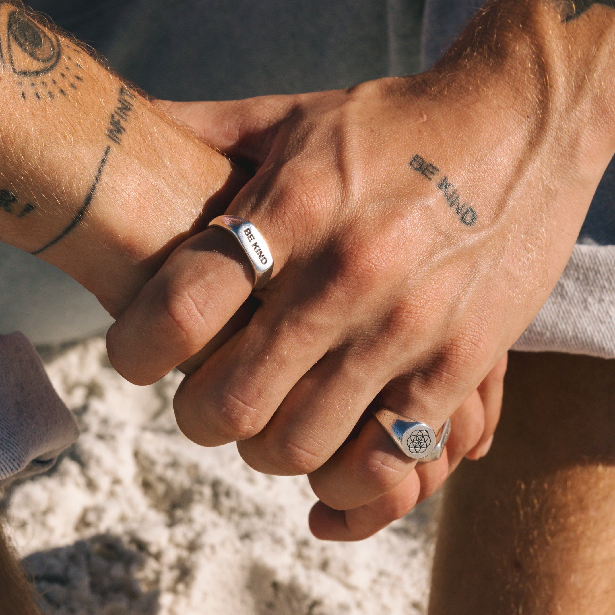 Close-up of two hands holding each other with tattoos and rings.