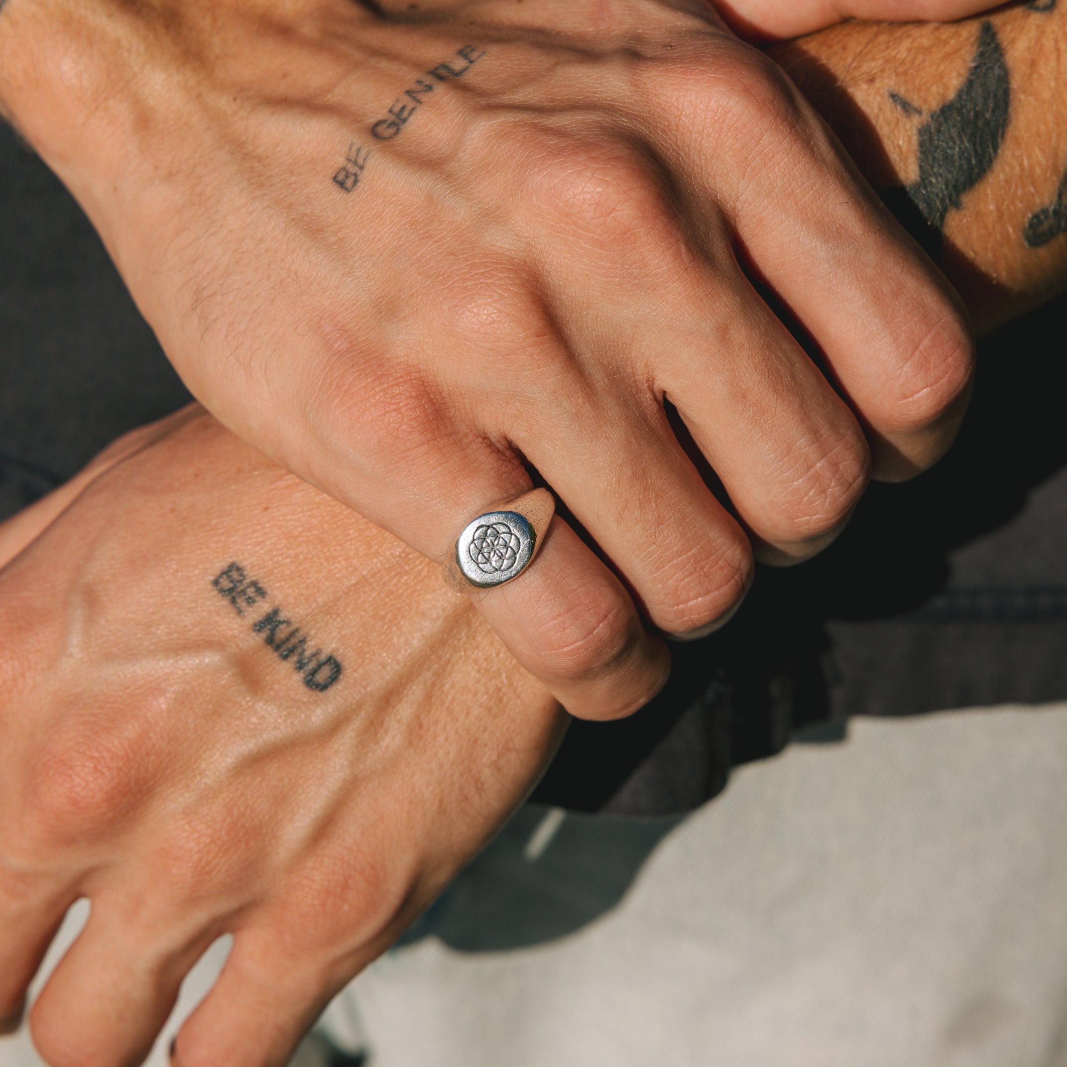 Close-up of a hand wearing a silver ring with a floral design, with tattoos on the fingers.