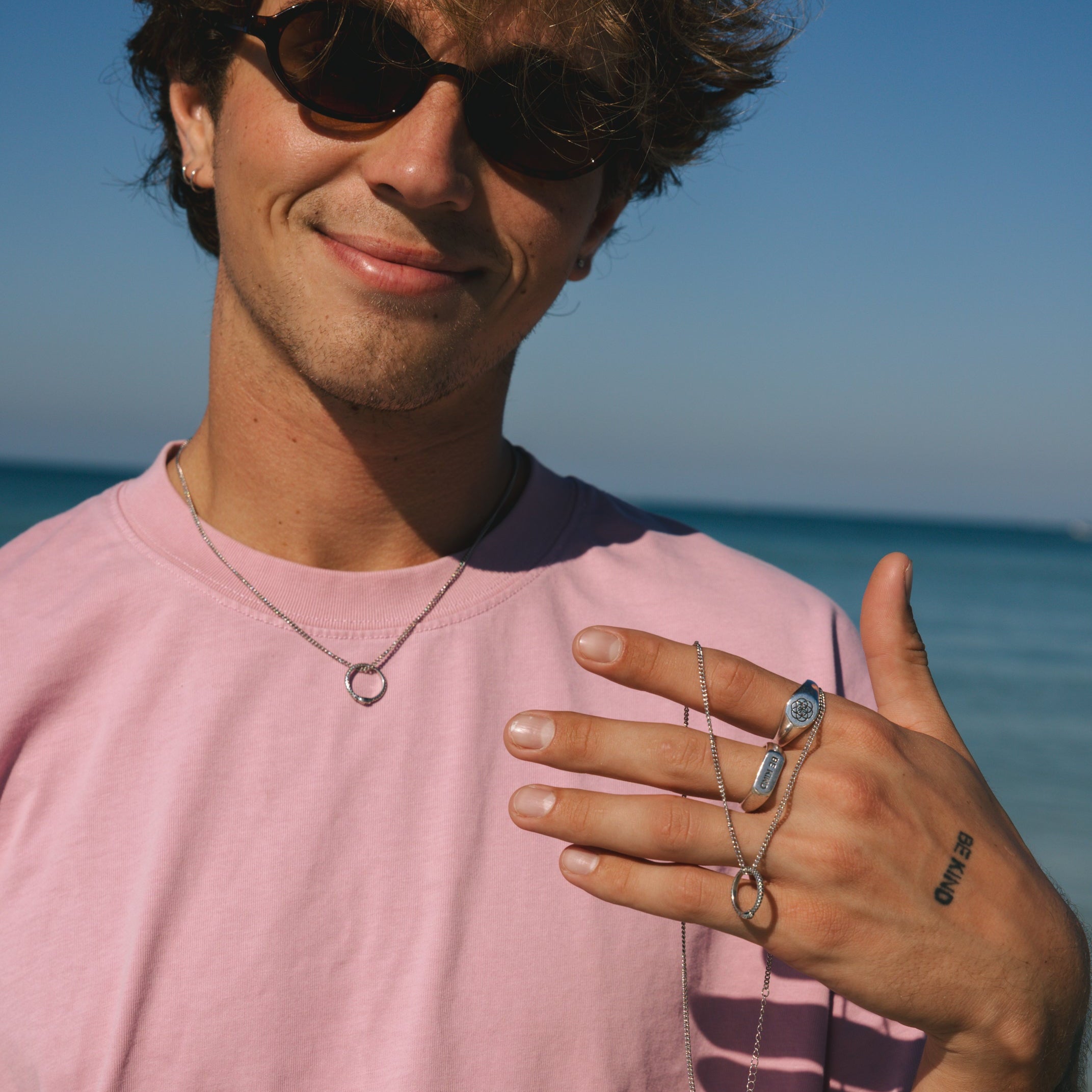 Man wearing sunglasses and a pink shirt with a clear blue sky and ocean background